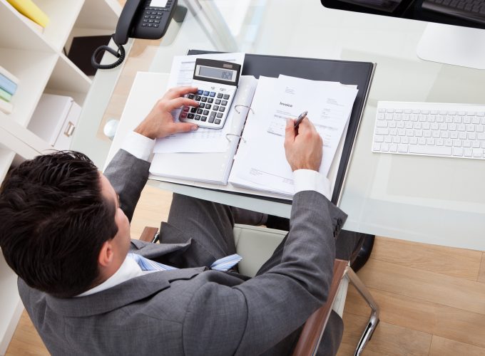 Businessman Calculating Documents Using Calculator In Office